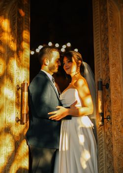 A beautiful bride and groom embracing near a detailed doorway under warm sunlight.