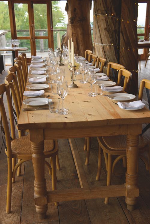 Free Long wooden dining table with elegant tableware set in a cozy rustic interior setting. Stock Photo