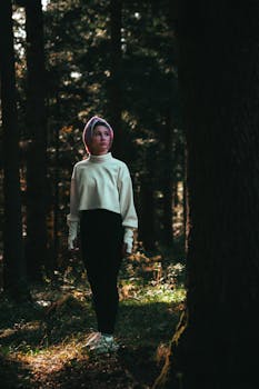 Moody portrait of a young woman in a dimly lit forest, exploring nature.
