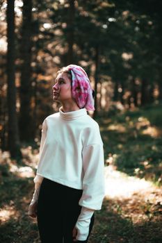 A woman with a pink headscarf walking through a sunlit forest, captured in a moody tone.