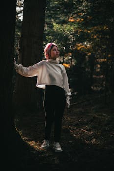 A thoughtful woman stands in a dimly lit forest. Moody and contemplative atmosphere.