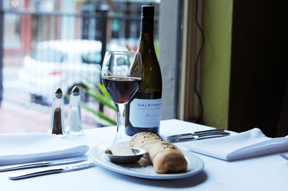 A stylish restaurant table featuring wine, bread, and condiments by a window.