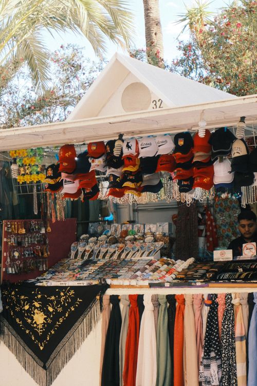 Free A vibrant street market stall selling hats, scarves, and souvenirs in a sunny outdoor setting. Stock Photo