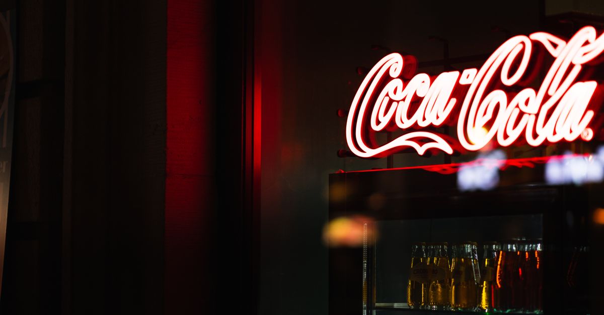 A group of friends laughing and holding giant colorful sodas outside a retro-style soda shop with neon signs