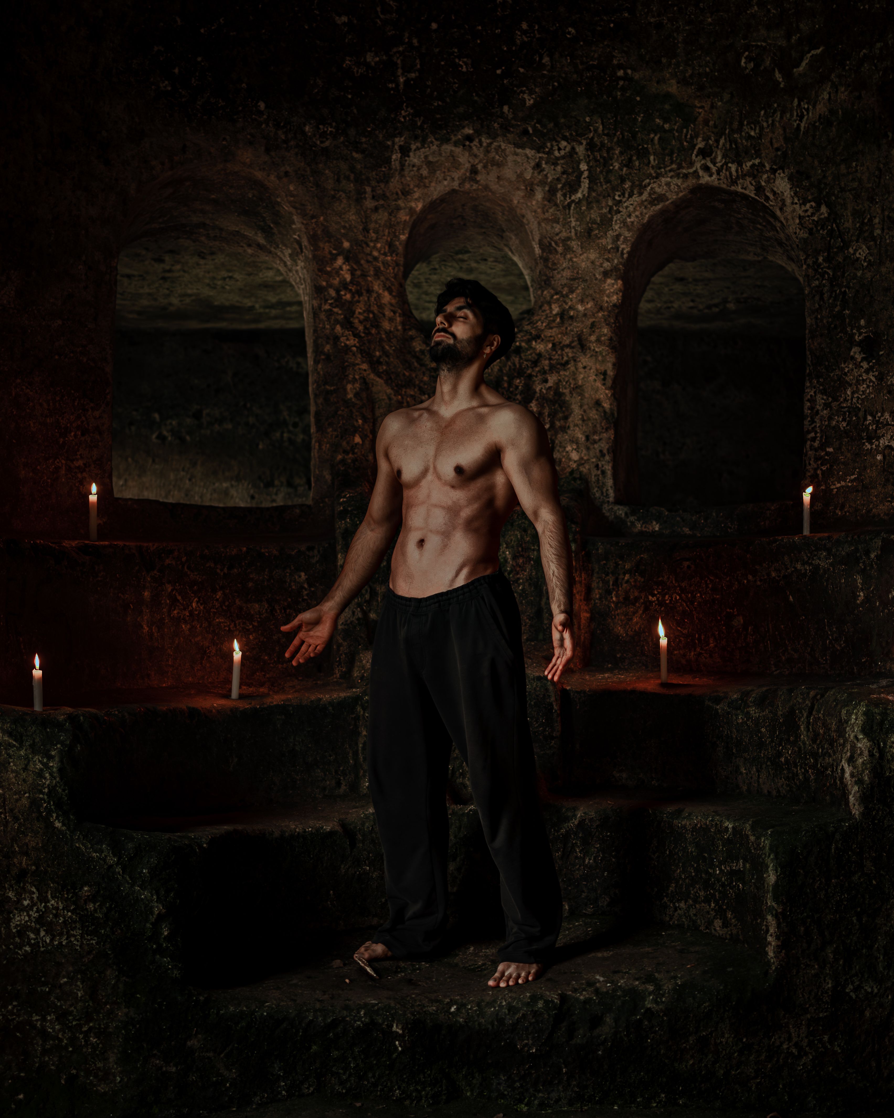 Man meditating in dimly lit space with candles