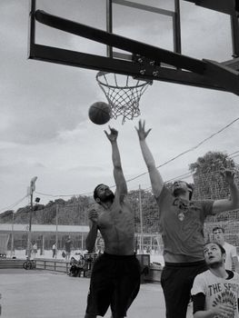 Intense basketball game with players jumping to score on an outdoor court.