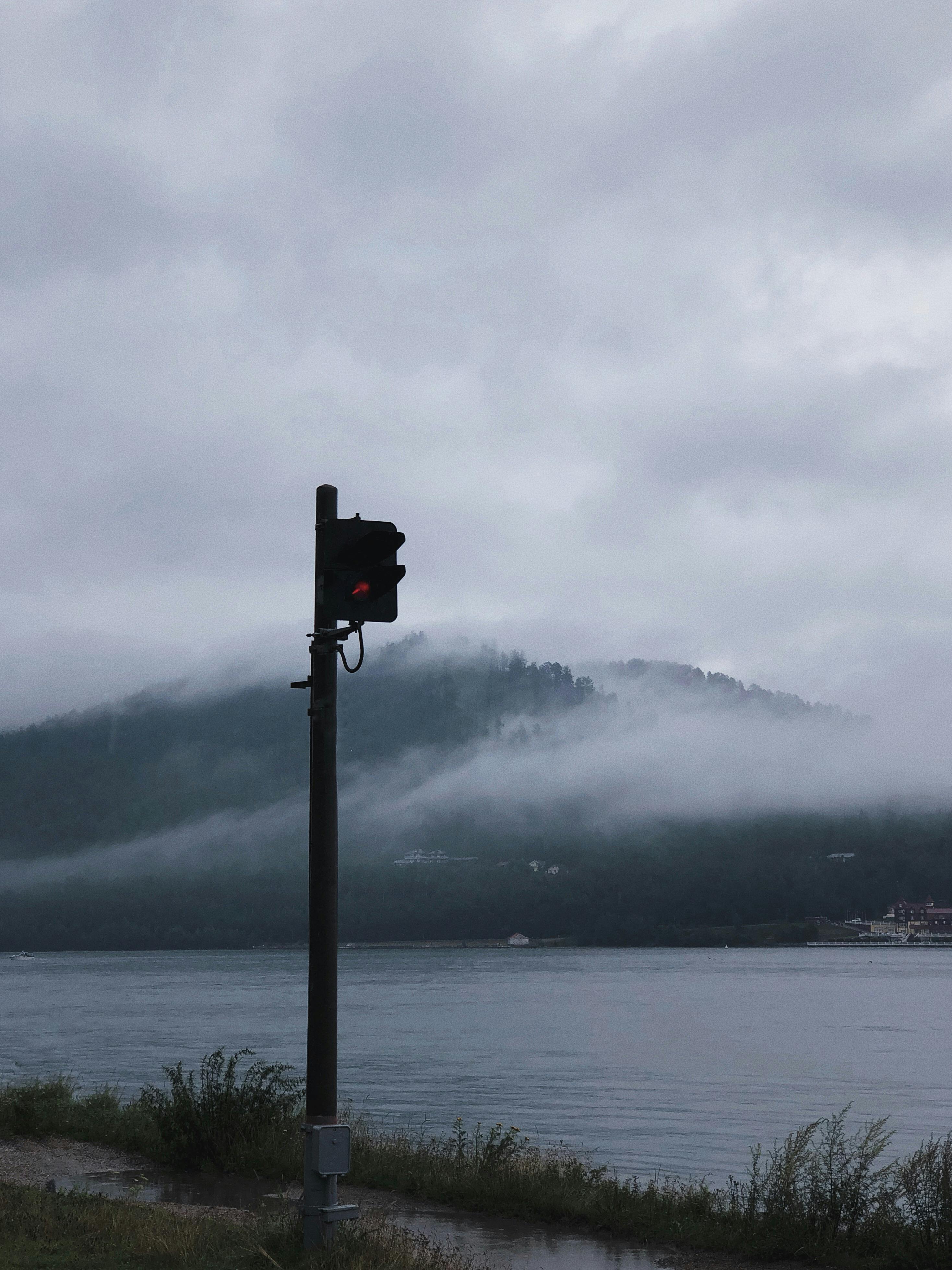 多云的天空下，平静的湖面与山丘间弥漫着诡异的雾气，唯有一个孤独的红绿灯矗立其中
