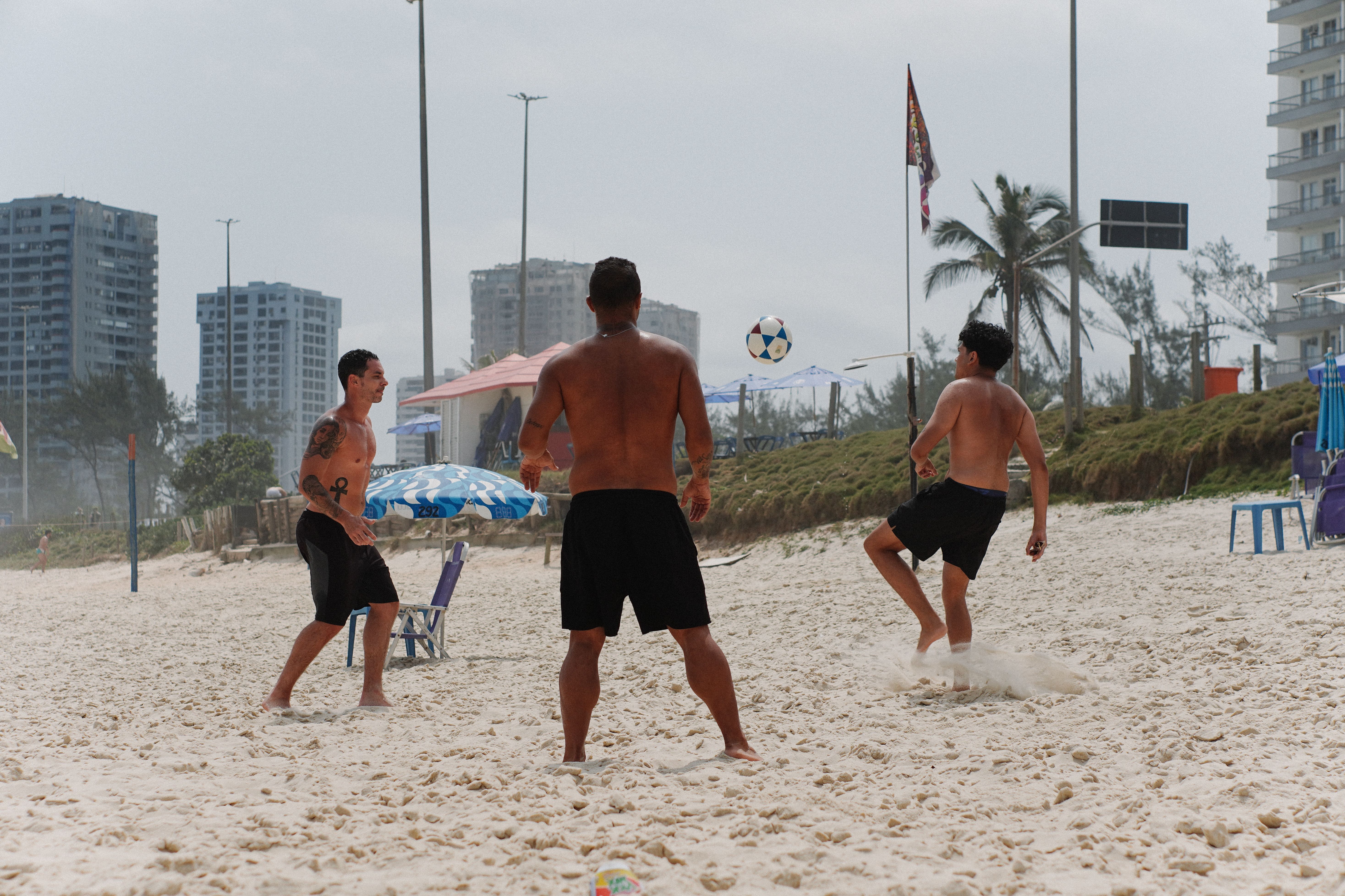 Gratis Strandfodboldkamp Med Tre Mænd På En Solskinsdag Lagerfoto