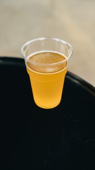 A clear plastic cup filled with refreshing golden beer on a dark surface.