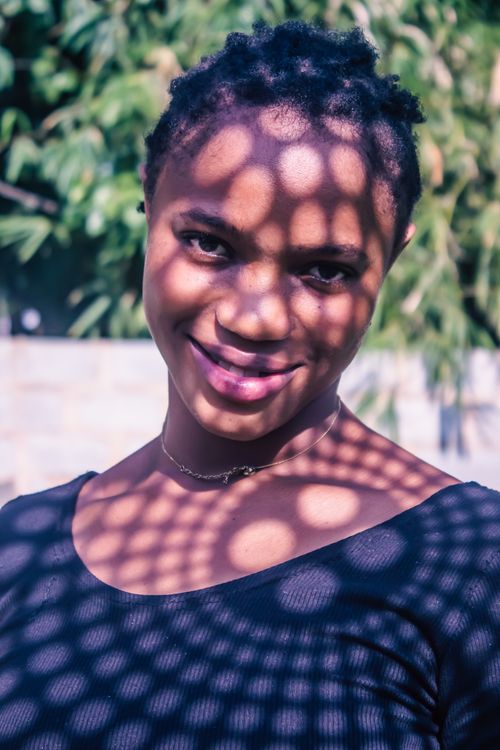 Free Smiling woman with intricate shadow patterns on face, creating an artistic outdoor portrait. Stock Photo