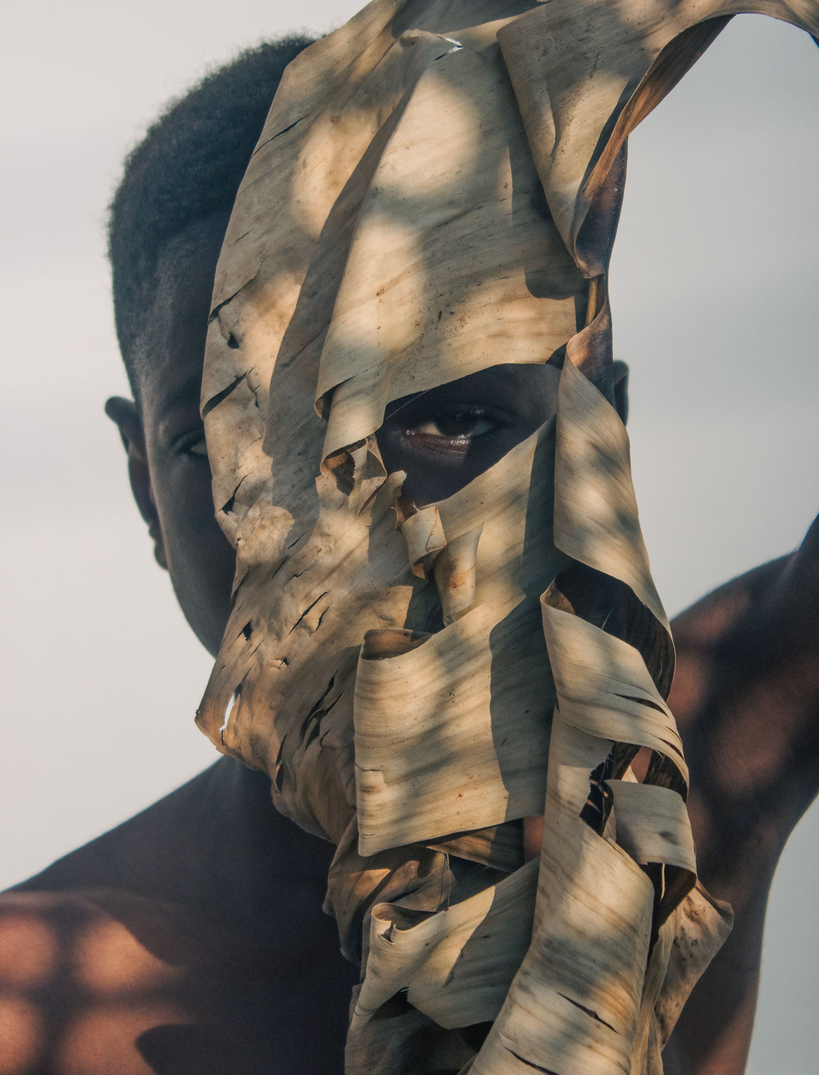 A captivating portrait featuring a person peering through a dried leaf, emphasizing natural textures and shadows.