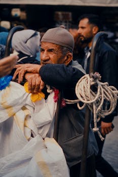 Elderly man resting on cart in bustling market, reflecting urban life.