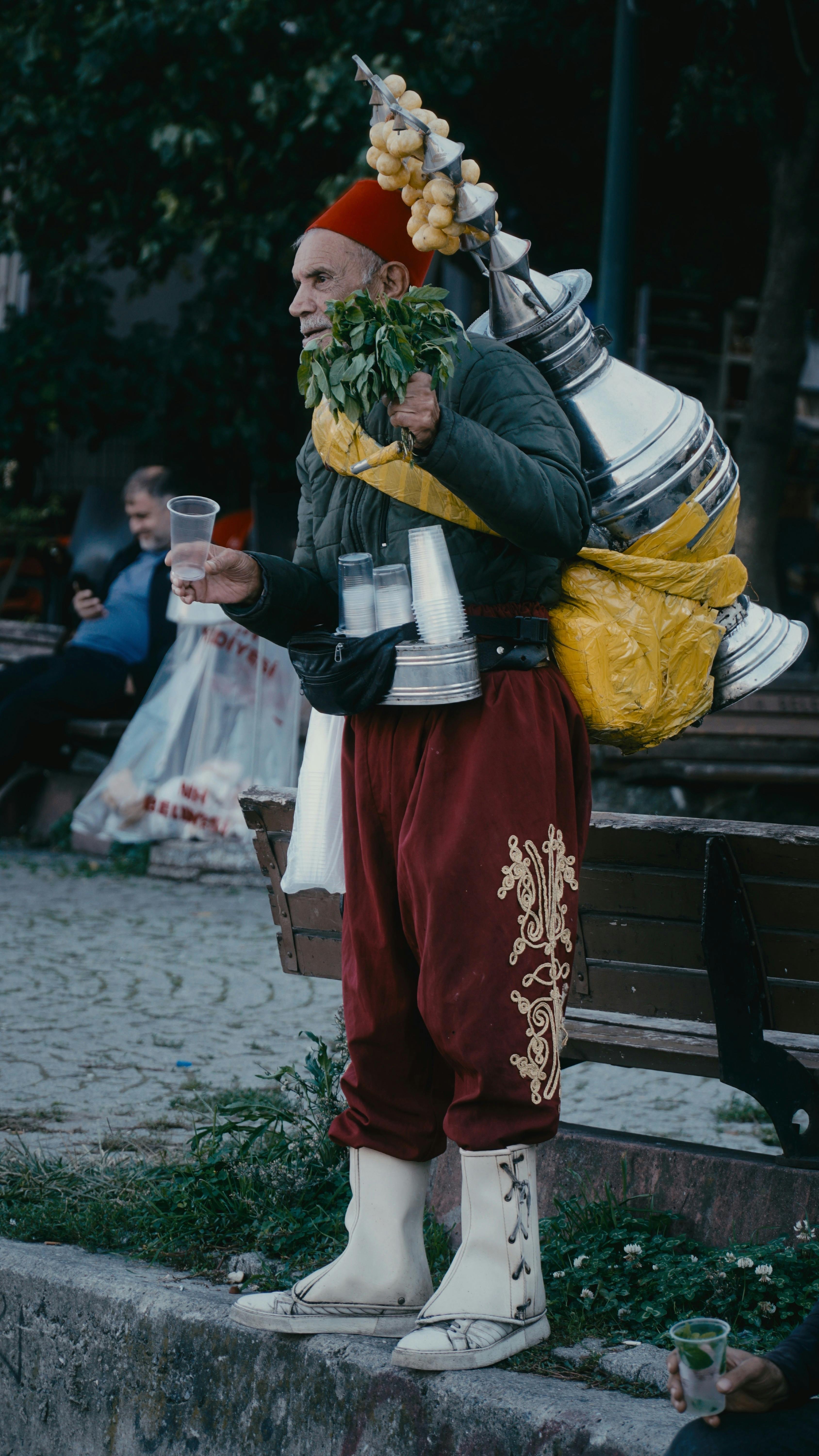 Street vendor in traditional attire with beverage equipment in a park.