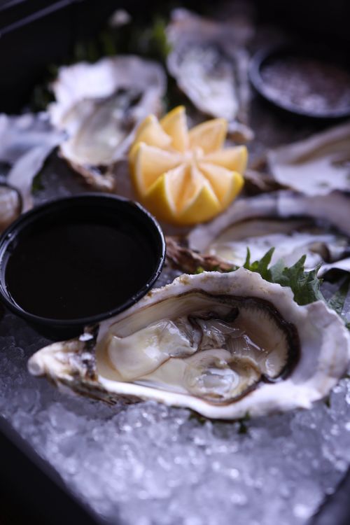 Free Close-up of fresh oysters on ice, served with lemon garnish and dipping sauce. Perfect seafood display. Stock Photo