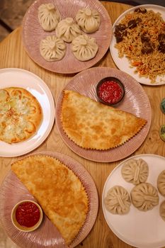 Top view of various traditional dishes with dumplings, cheburek, and pilaf.