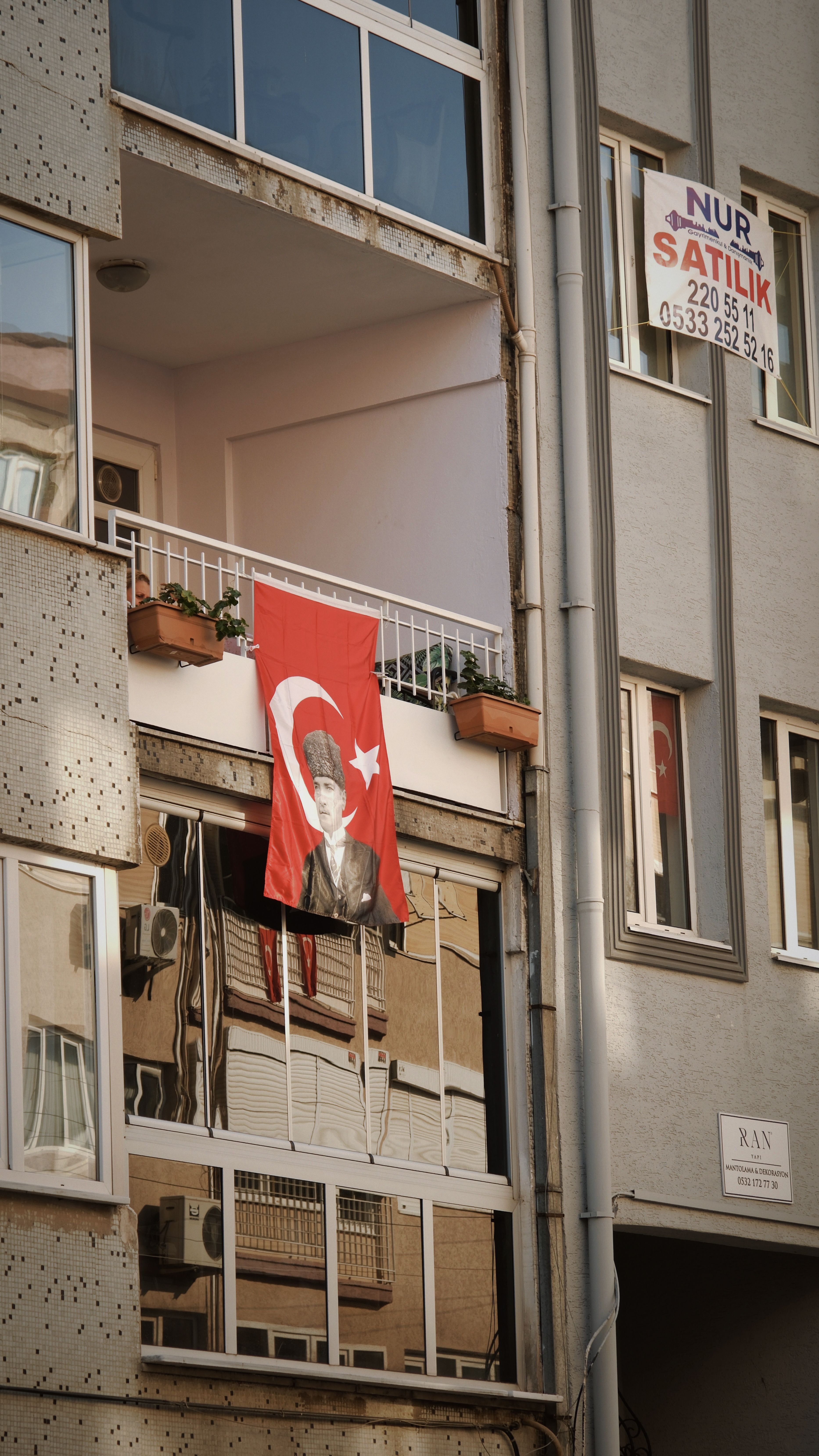 A Turkish flag with Atatürk's portrait displayed on a residential balcony in Türkiye.