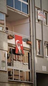 A Turkish flag with Atatürk's portrait displayed on a residential balcony in Türkiye.