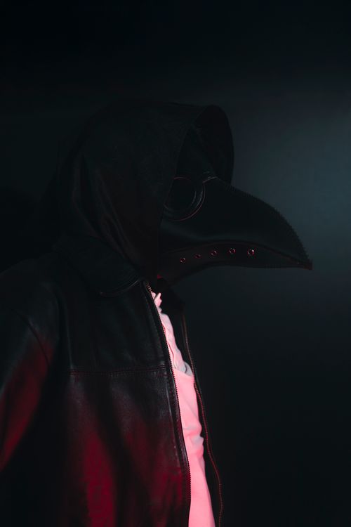 Free A person in a dark plague doctor costume and hood, lit dramatically. Stock Photo