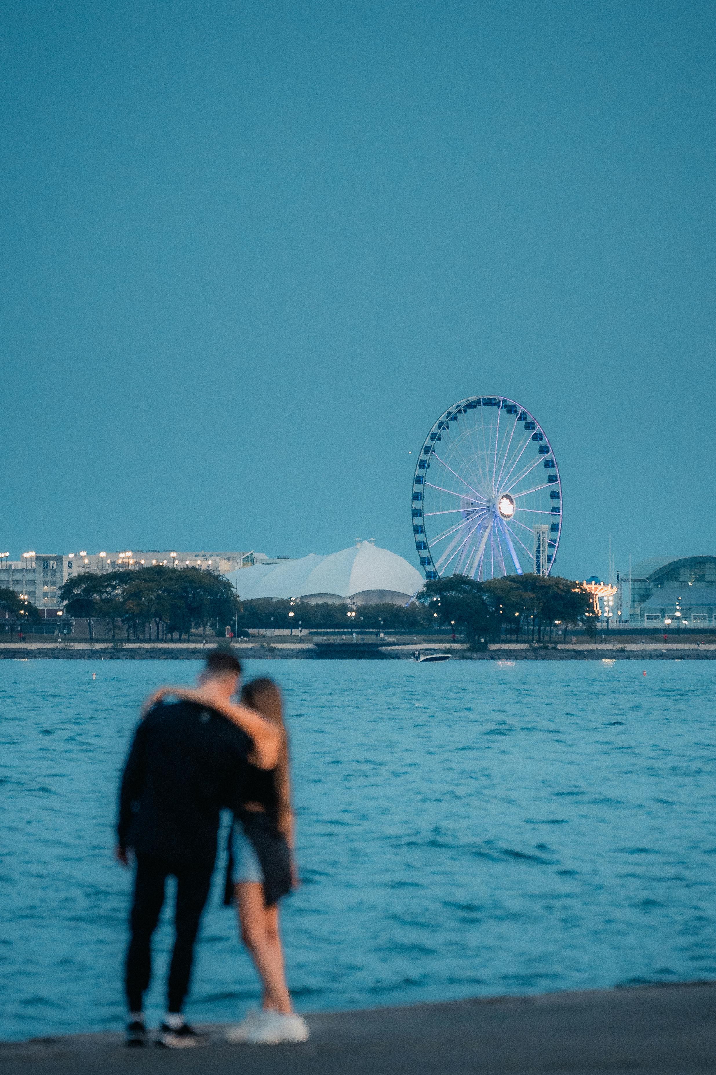 Couple enjoying a romantic evening by the waterfront with a Ferris wheel in the background.