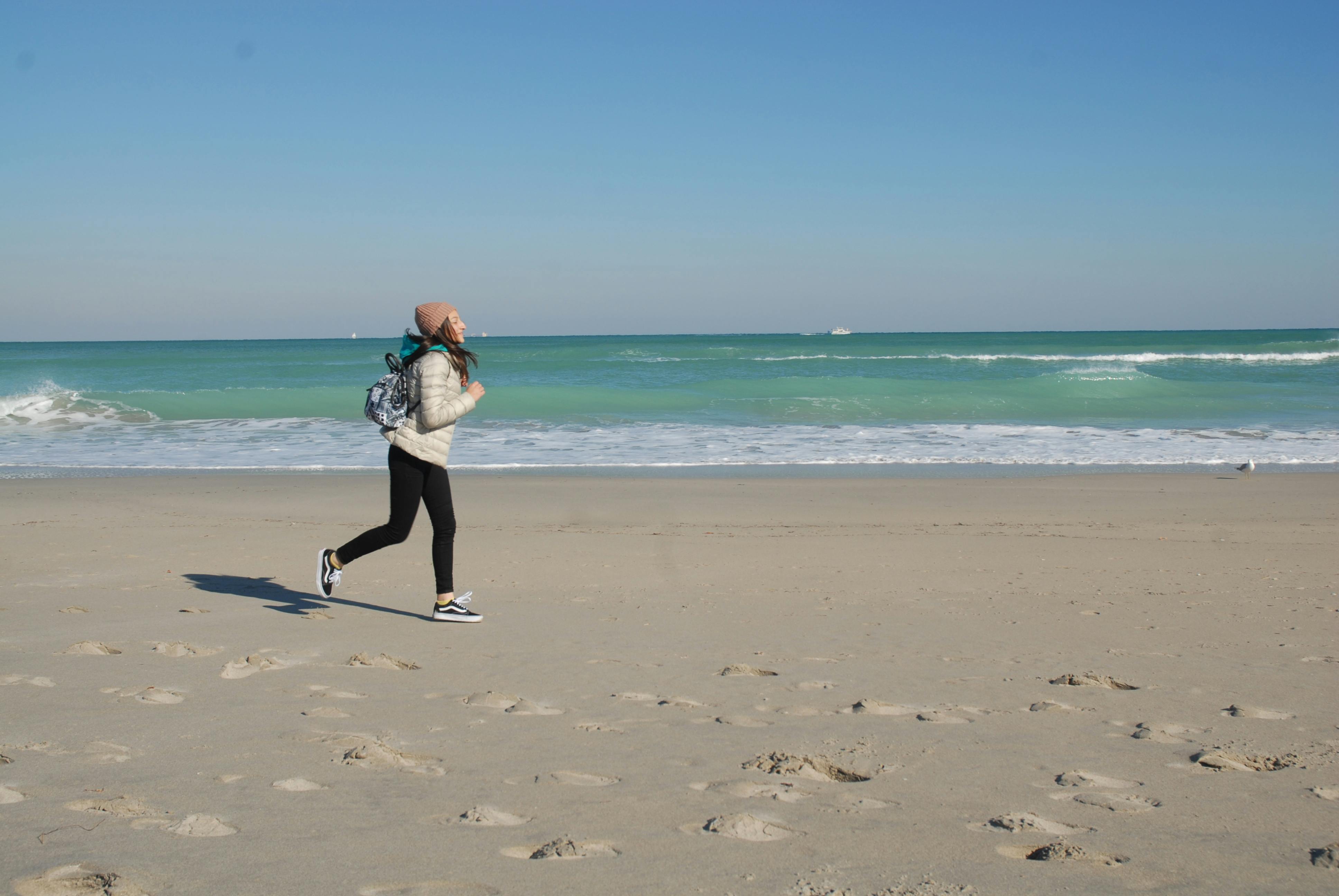 Active woman jogging on a sunny Miami beach with clear skies and turquoise waters.