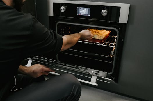 A chef placing a pasta bake into an oven in a modern kitchen setting.