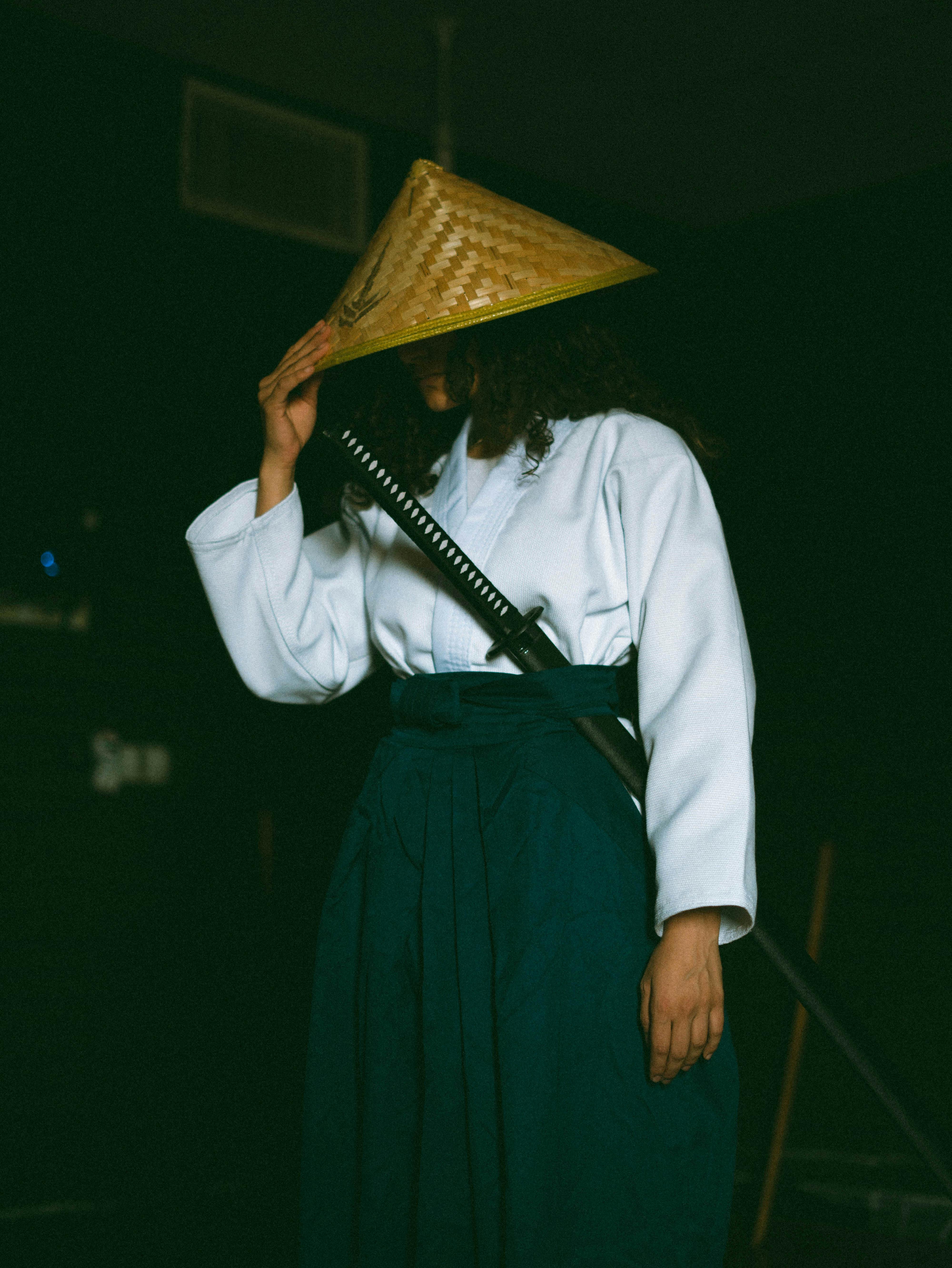 A person dressed as a samurai in traditional attire, holding a katana with a straw hat.