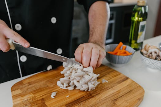 Close-up of a chef cutting white mushrooms on a wooden board in a kitchen setting.