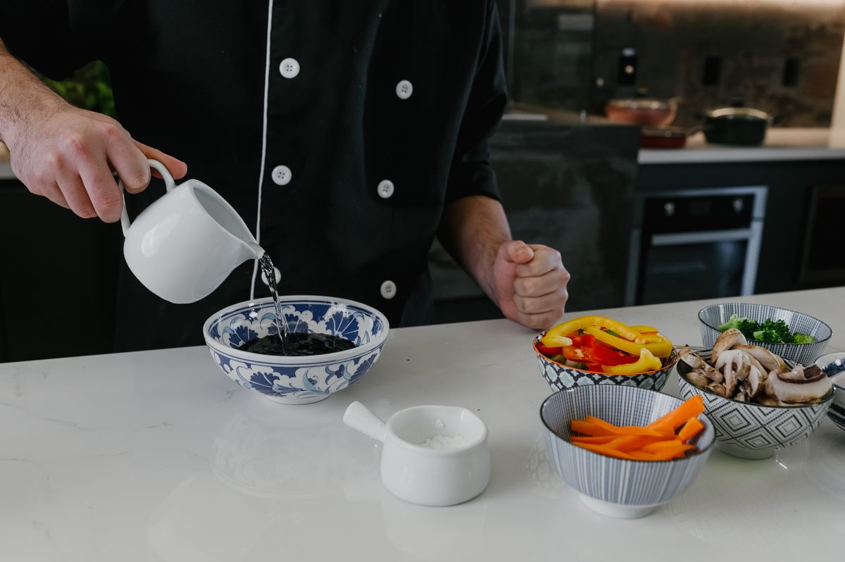 A cook adds water to a dish of prepped vegetables — photo by Jonathan Borba on Pexels