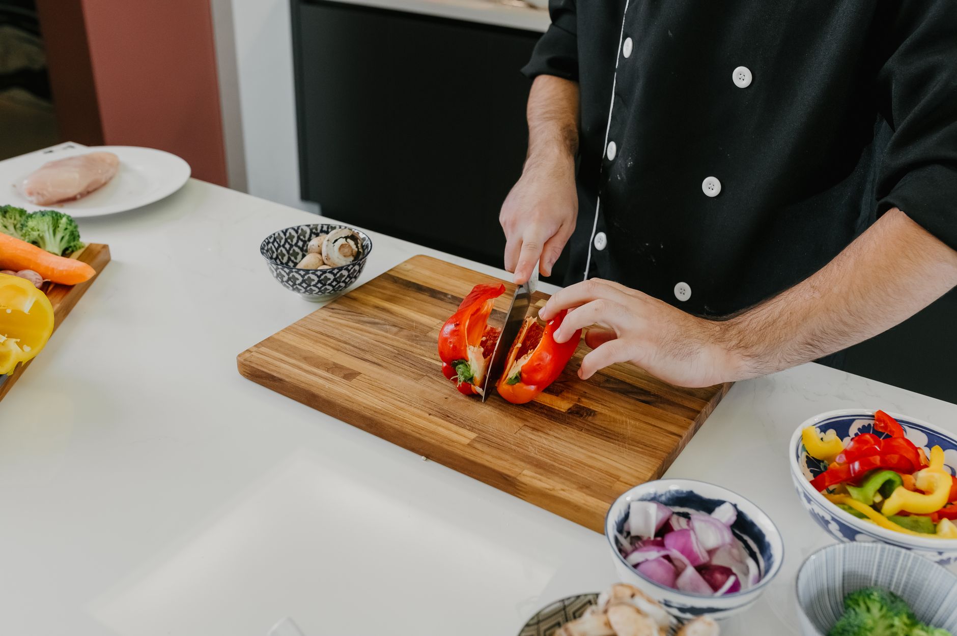 Chef slicing fresh bell peppers on a wooden board in a modern kitchen.