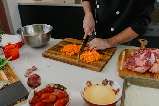 Chef chops carrots on a cutting board surrounded by fresh ingredients in a modern kitchen.