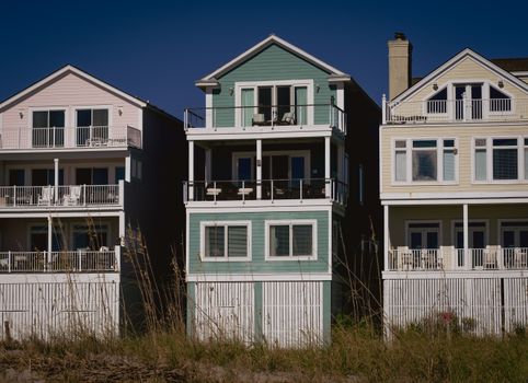 Sunny day view of colorful coastal homes with wooden siding and balconies, perfect for summer living.