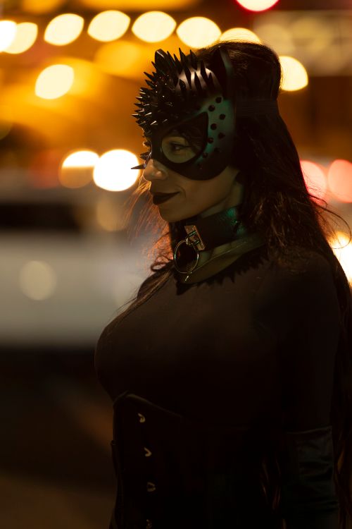 Free Side profile of a woman wearing a spiked mask in a nighttime urban setting with bokeh lights. Stock Photo