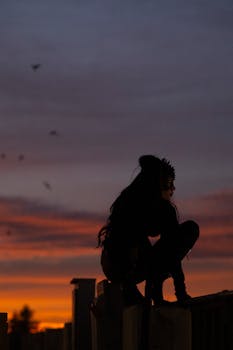 A mysterious silhouette of a woman crouching at sunset with a dramatic sky.