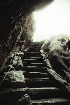 Moody stone stairway leading from a dim cave environment into bright daylight.