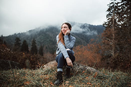Portrait of a woman sitting on a rock, surrounded by misty autumn mountains and forests.