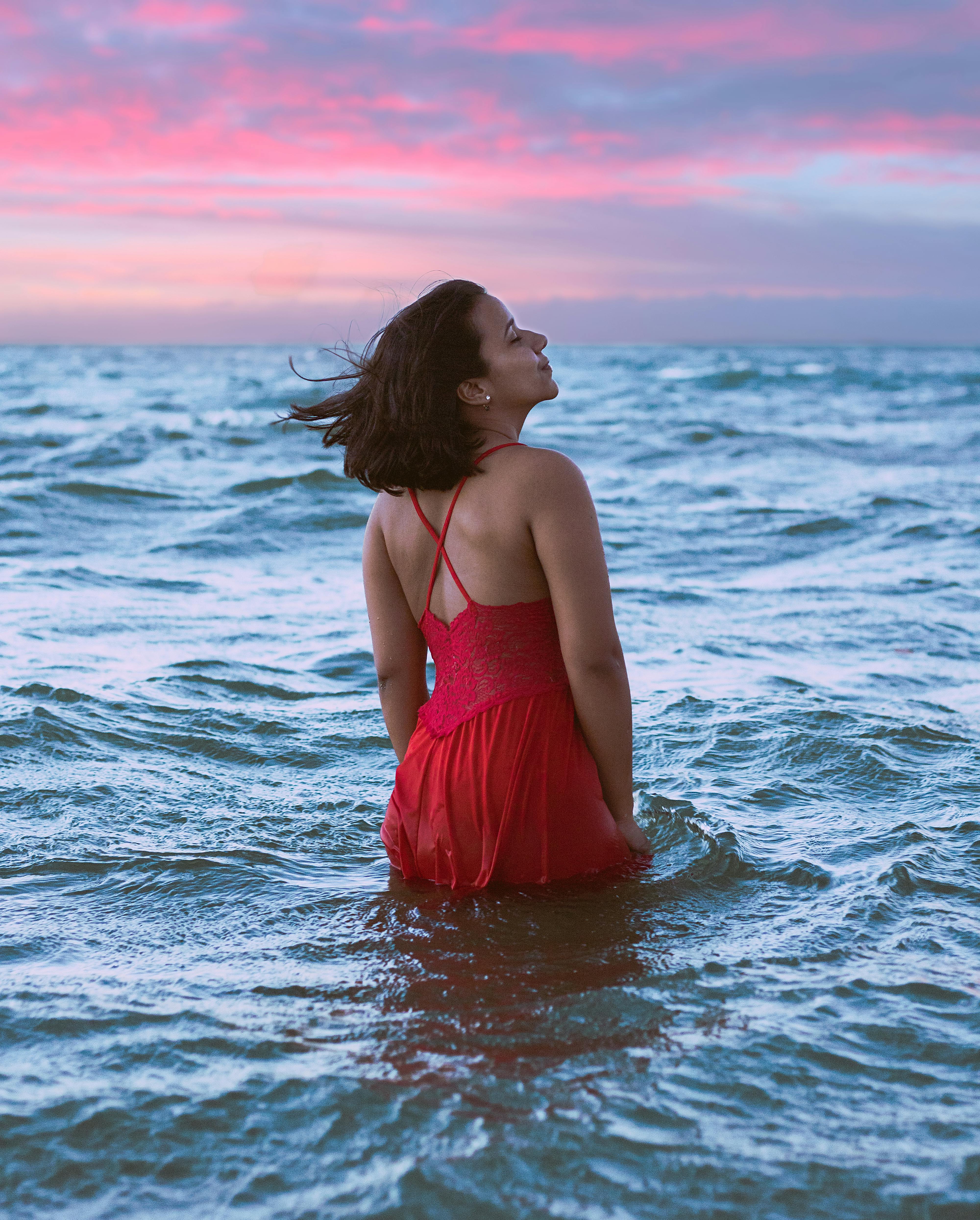 日落时分，一位身着红色连衣裙的女子在海中享受着宁静的时刻