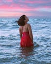 日落时分，一名身穿红色连衣裙的女子在大海中享受宁静的时刻