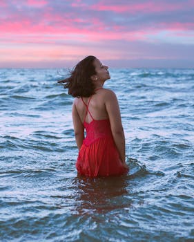 日落时分，一位身着红色连衣裙的女子在海中享受着宁静的时刻