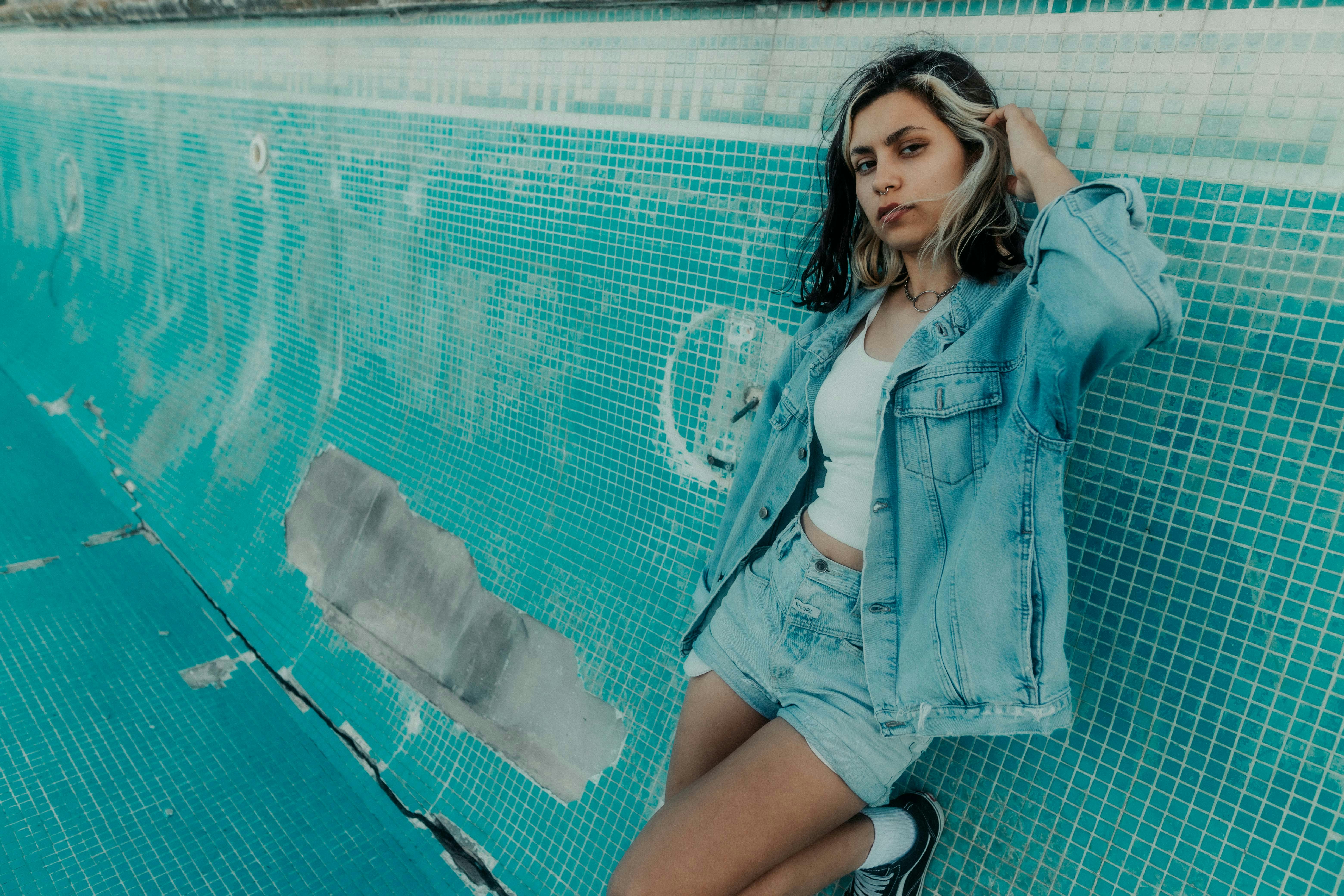 Young woman in denim outfit posing by an empty pool, conveying urban style.