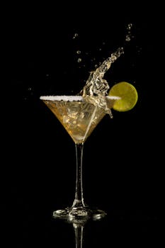 Martini glass with a splash of liquid and lime garnish on black background.