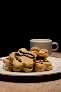 Mouth-watering flower-shaped cookies adorned with chocolate drizzle on a plate with coffee.