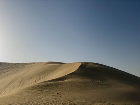 A breathtaking view of golden sand dunes under a clear blue sky in a tranquil desert landscape.