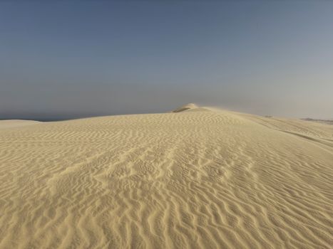 Serene desert landscape with golden sand dunes under clear blue sky at sunrise.