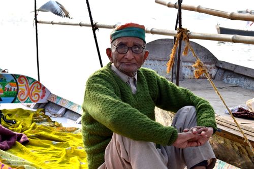 Free Senior man in a green sweater sitting on a boat with bright textiles, outdoors. Stock Photo