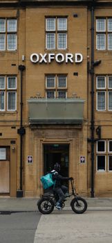 Biker passing in front of Oxford building with classic architecture.