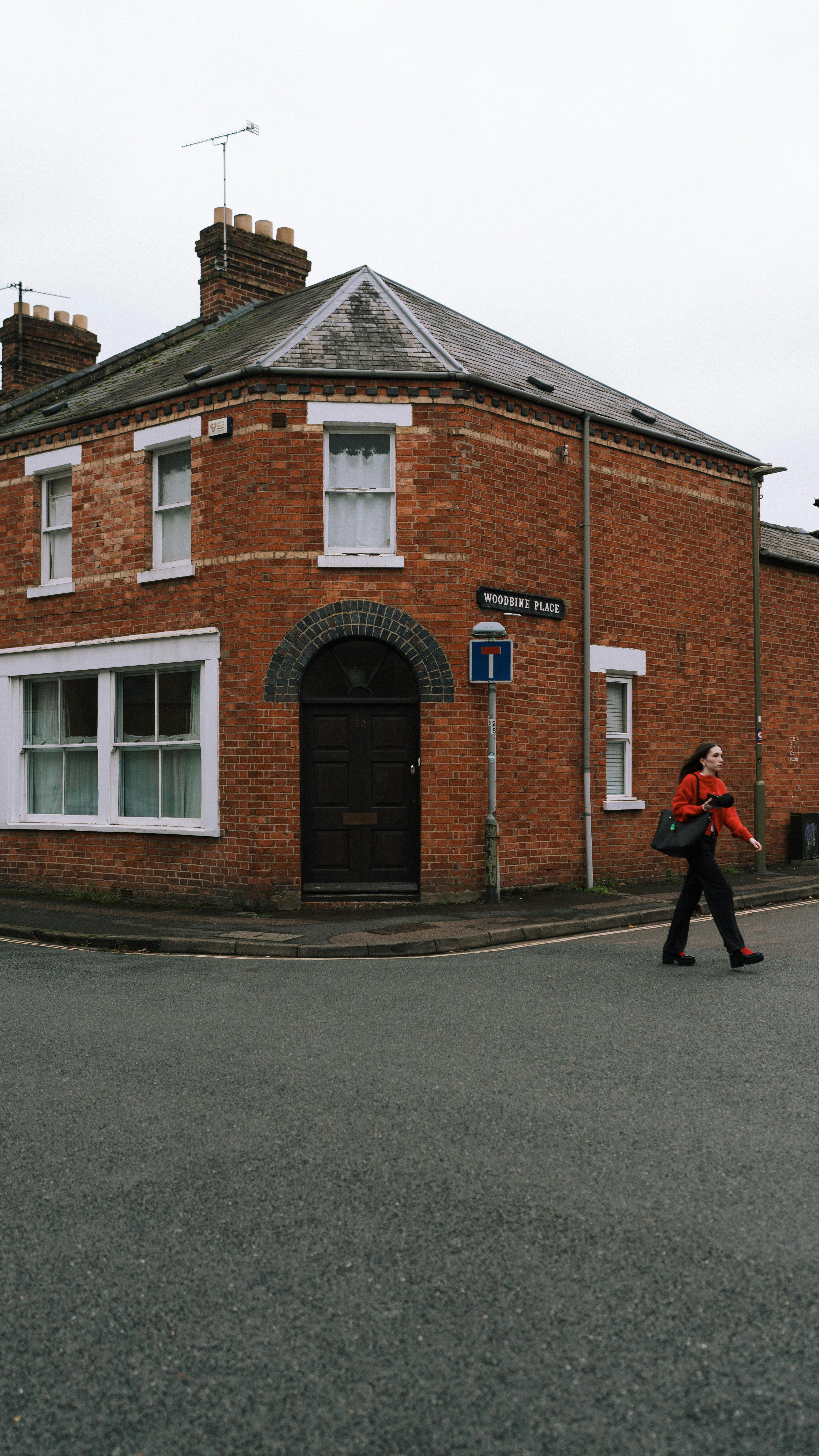 Free A person walks past a historic red brick building on a quiet street corner. Stock Photo
