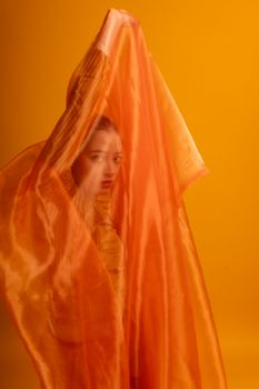 A creative portrait of a female dancer enveloped in orange fabric, highlighting vibrant expression.