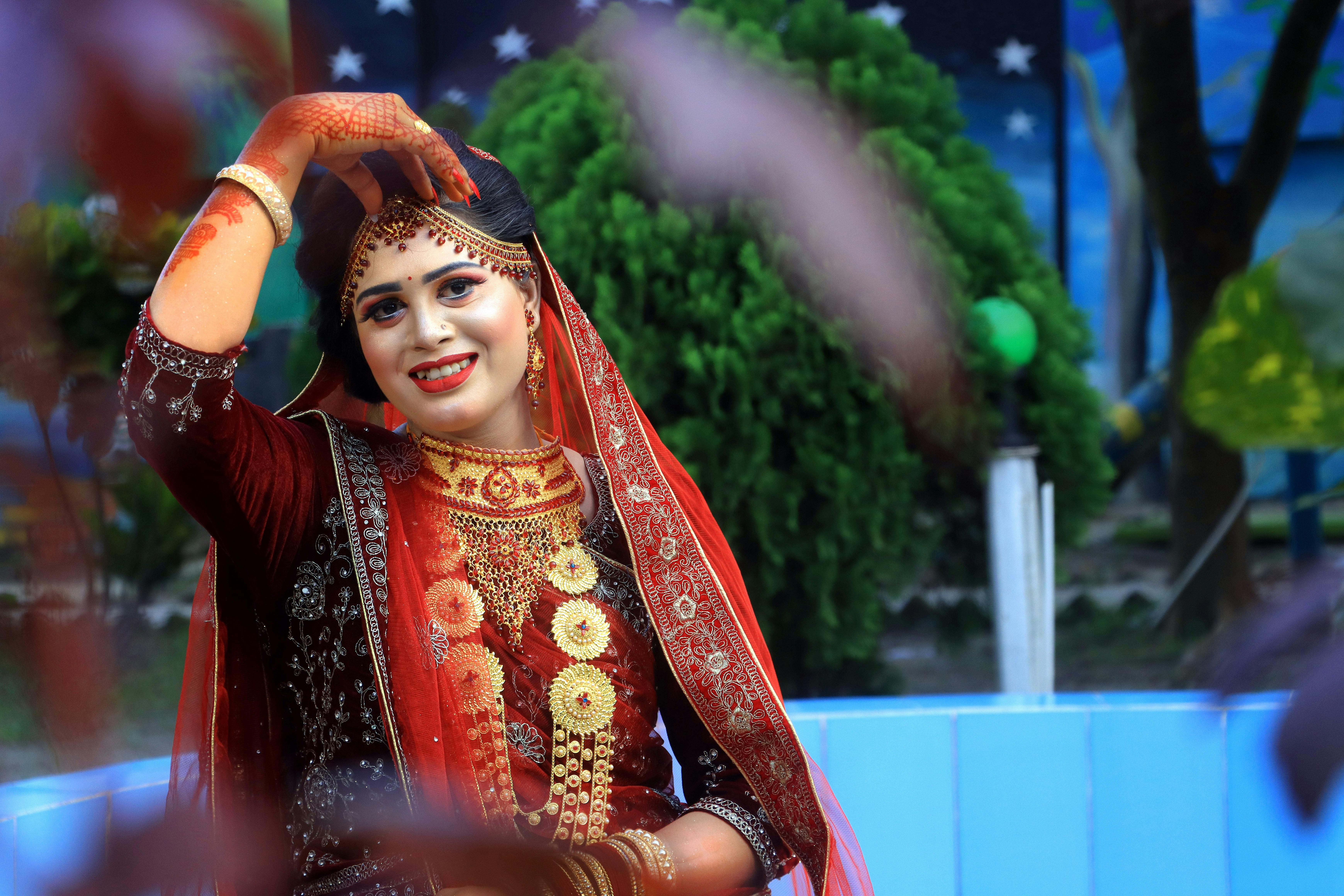 A stunning bride wearing intricate traditional attire poses outdoors with vibrant surroundings.