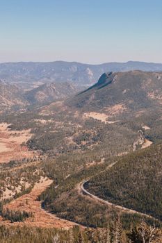 Aerial view of a scenic mountain range with a winding road through a forest.