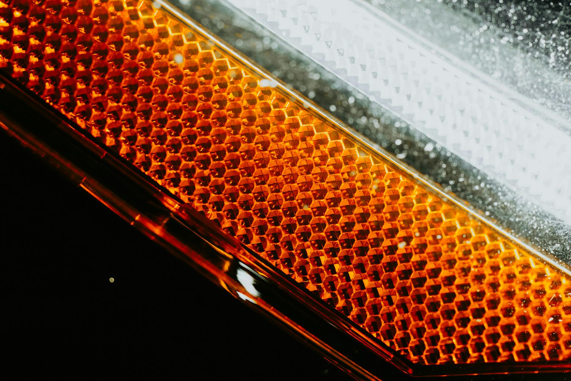 Detailed view of a car headlight with an orange and white honeycomb pattern illuminating.